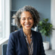 A smiling diverse woman posing for a professional headshot in a clean, brightly lit environment with soft blue tones.