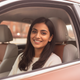Candid portrait of a smiling South Asian woman in a car, looking at the viewer with a happy and satisfied expression.