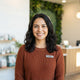 A friendly, diverse pet owner smiling warmly in a professional, well-lit portrait setting with neutral forest green and cream